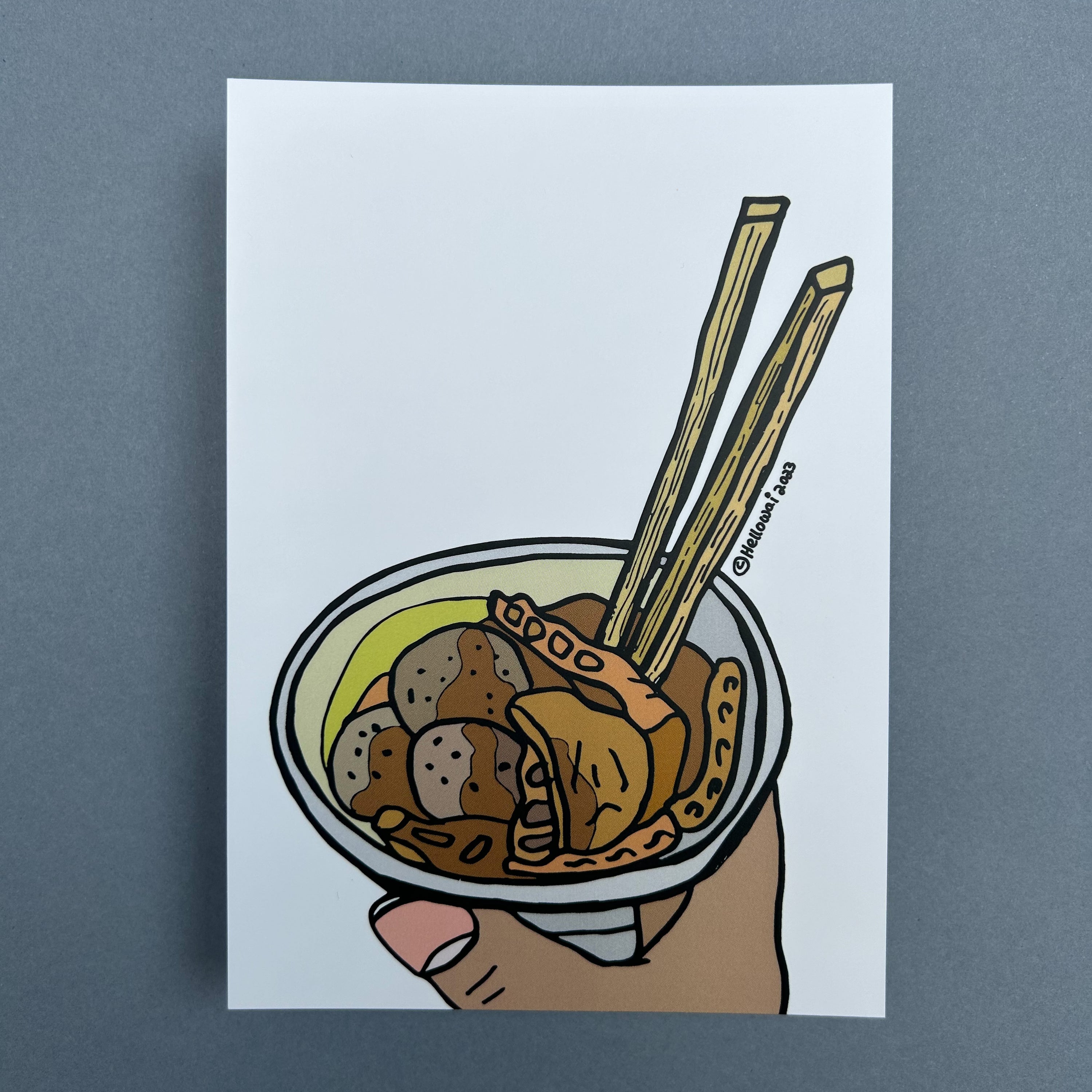 An A6 Hello Wai flat notecard with a colour illustration of a hand holding a cup of curry fish ball and a pair of chopsticks, printed on white card.