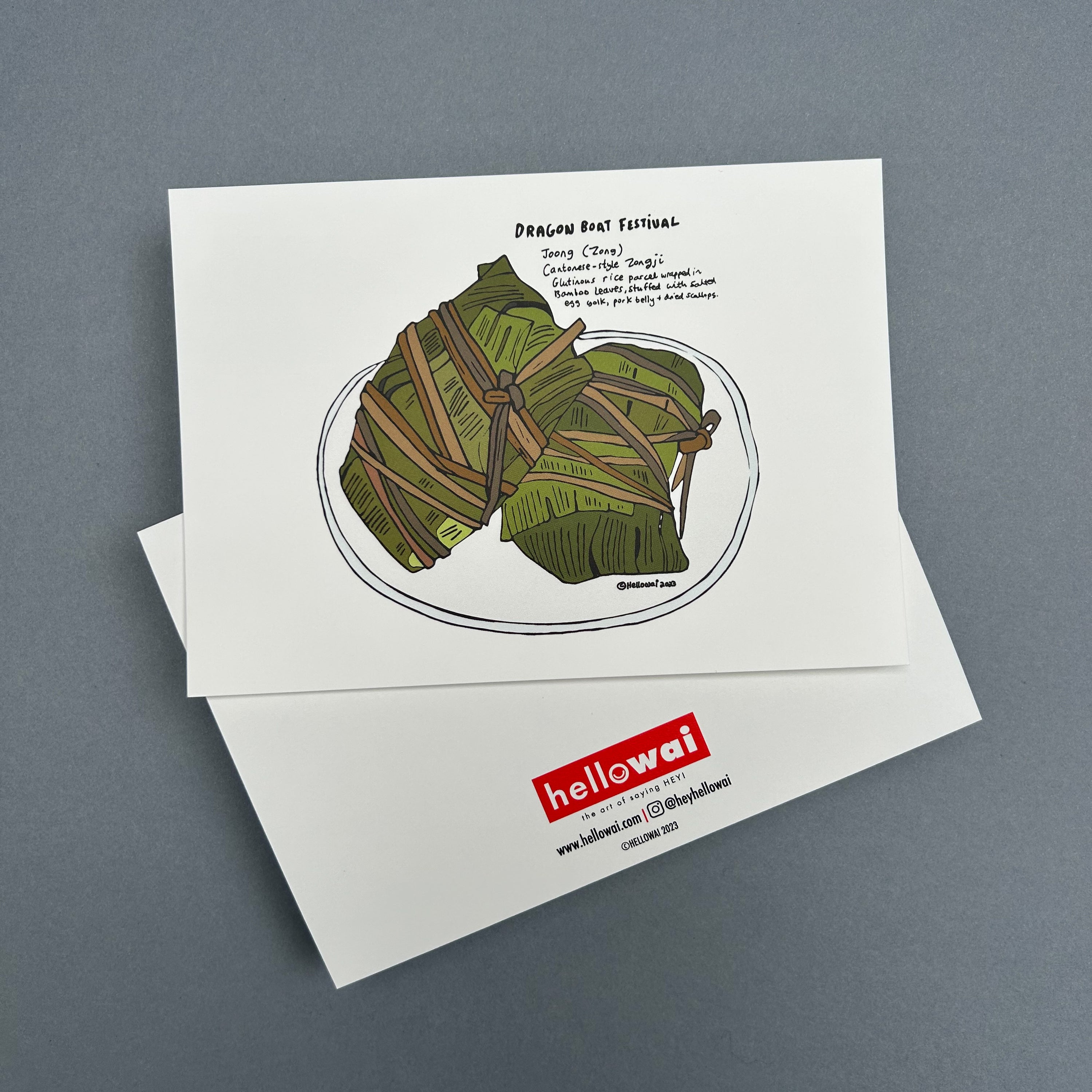 Front and back view of an A6 Hello Wai flat notecard. Front has colour illustration of a two glutinous rice parcels wrapped in bamboo leaves on a plate and some handwritten text describing a Dragon Boat Festival food tradition. Back has the Hello Wai logo.