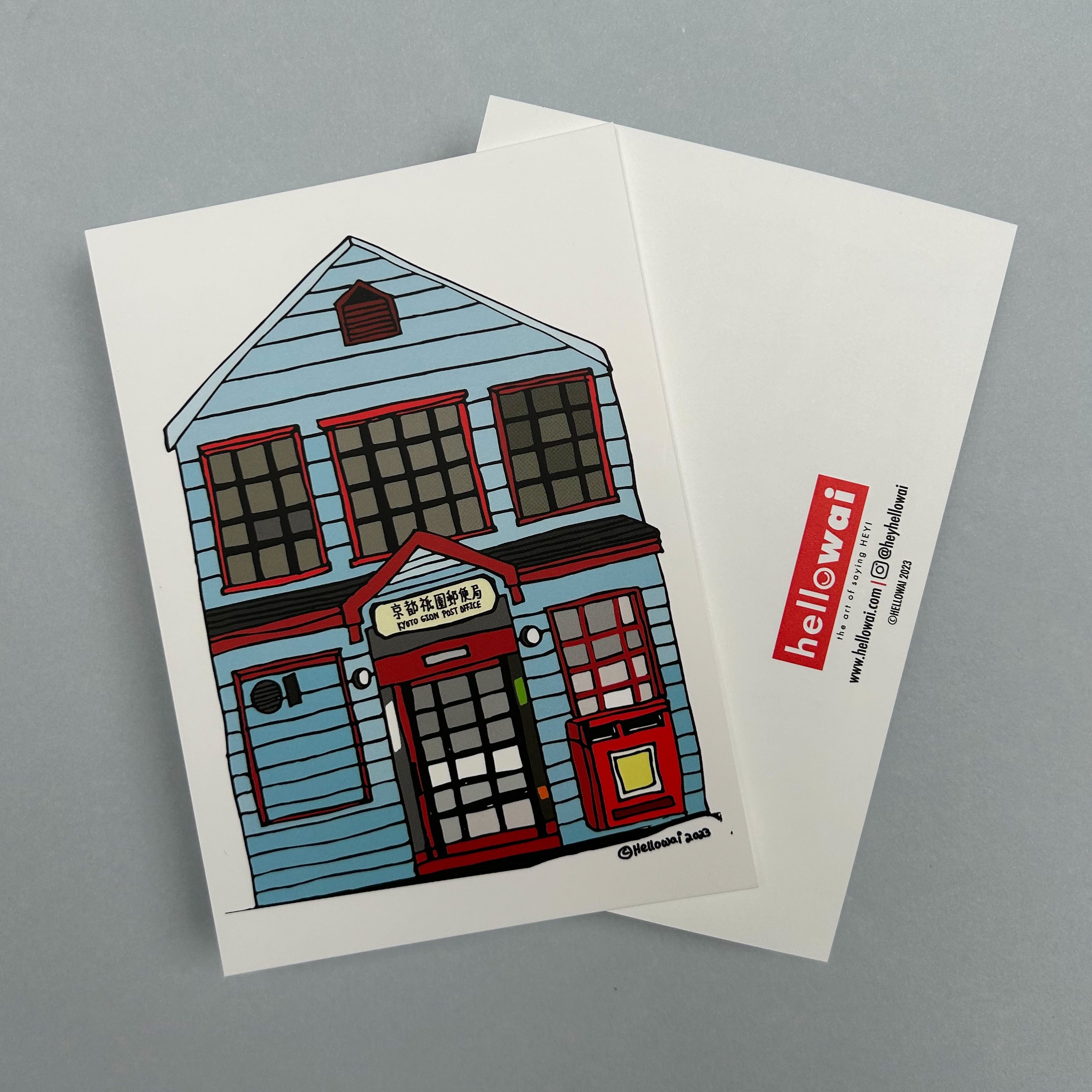 Front and back view of an A6 Hello Wai flat notecard. Front has colour illustration of a light blue building with a sign saying Kyoto Gion Post Office above the front door. Back has the Hello Wai logo.