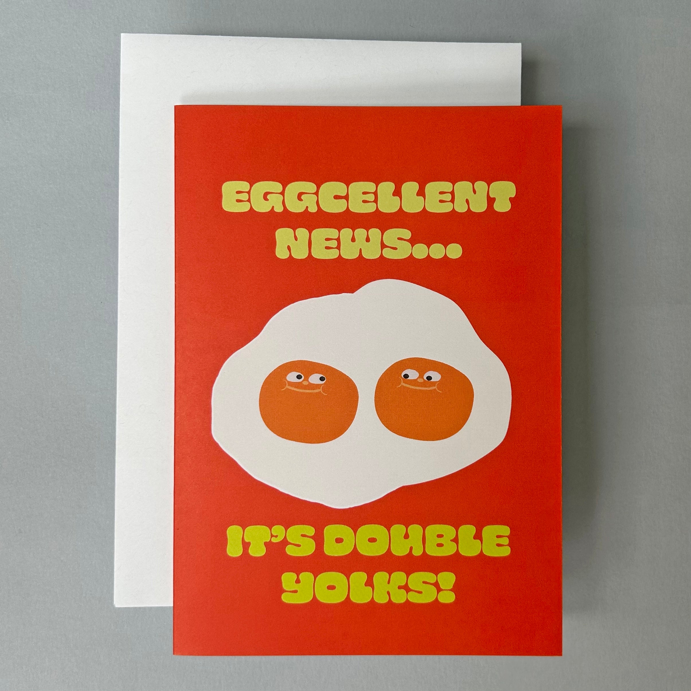 BRight red greeting card with cartoon style illustration of double yolk eggs and text: Eggcellent News...It's Double Yolk!" in yellow. 