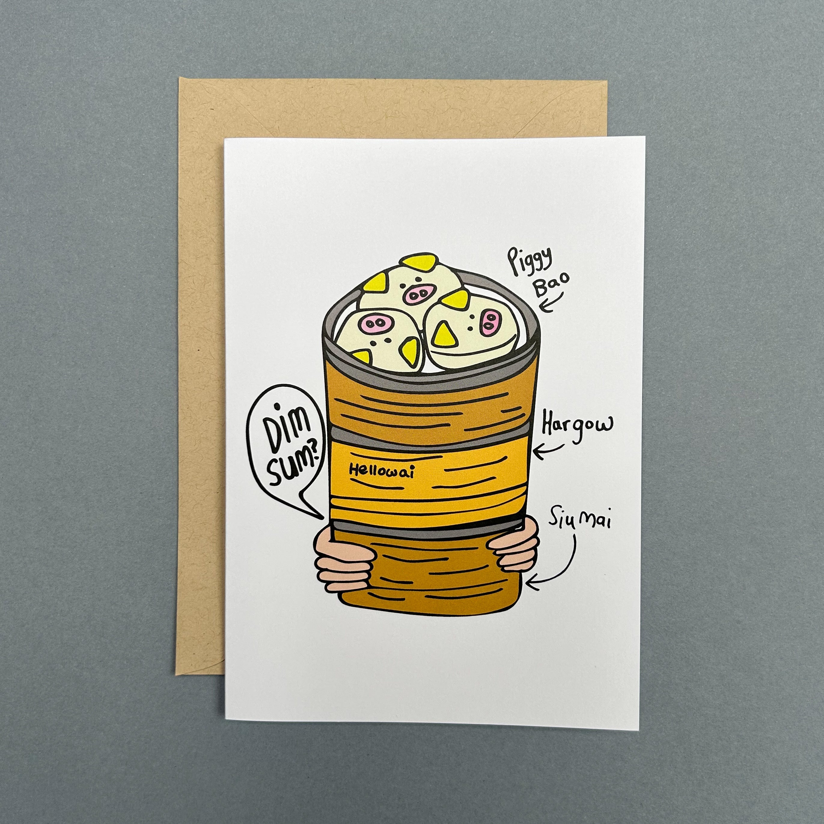 An A6 Hello Wai folded greeting card with a colour illustration of a pair of hands carrying three bamboo baskets stacked with dim sum, the top basket has pig shaped bao, printed on white card. The card is placed on top of a brown envelope.