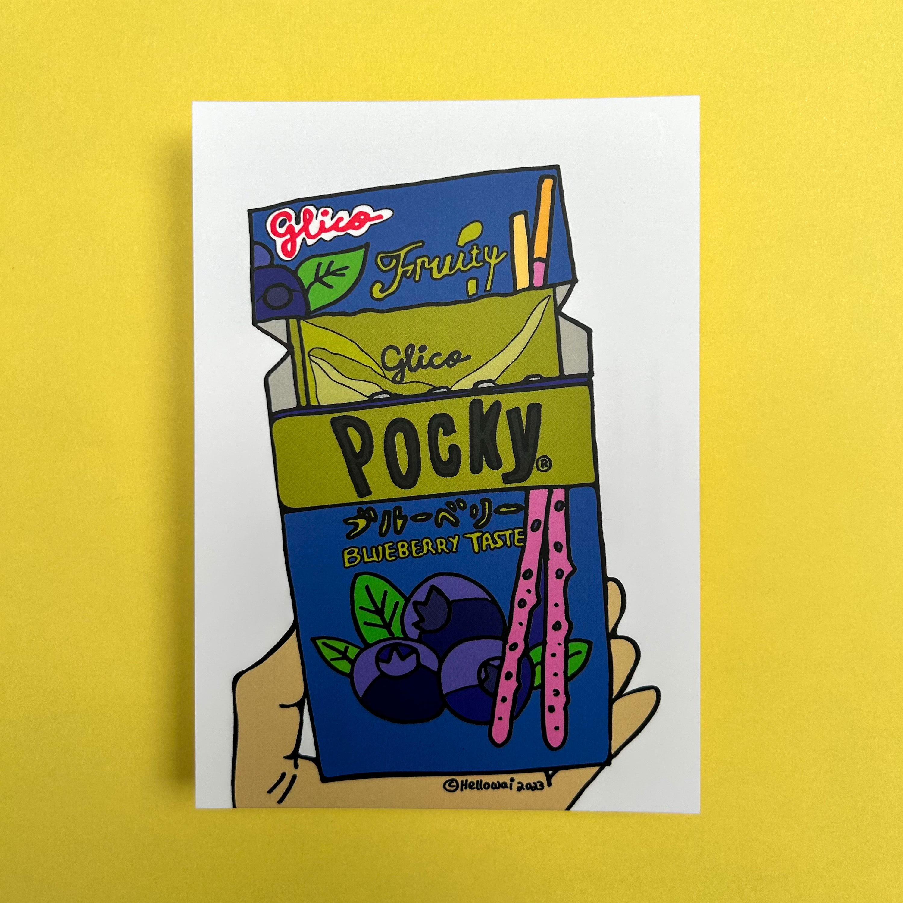 An A6 Hello Wai flat notecard with a colour illustration of a hand holding an opened box of Blueberry Taste Pocky, printed on white card. 