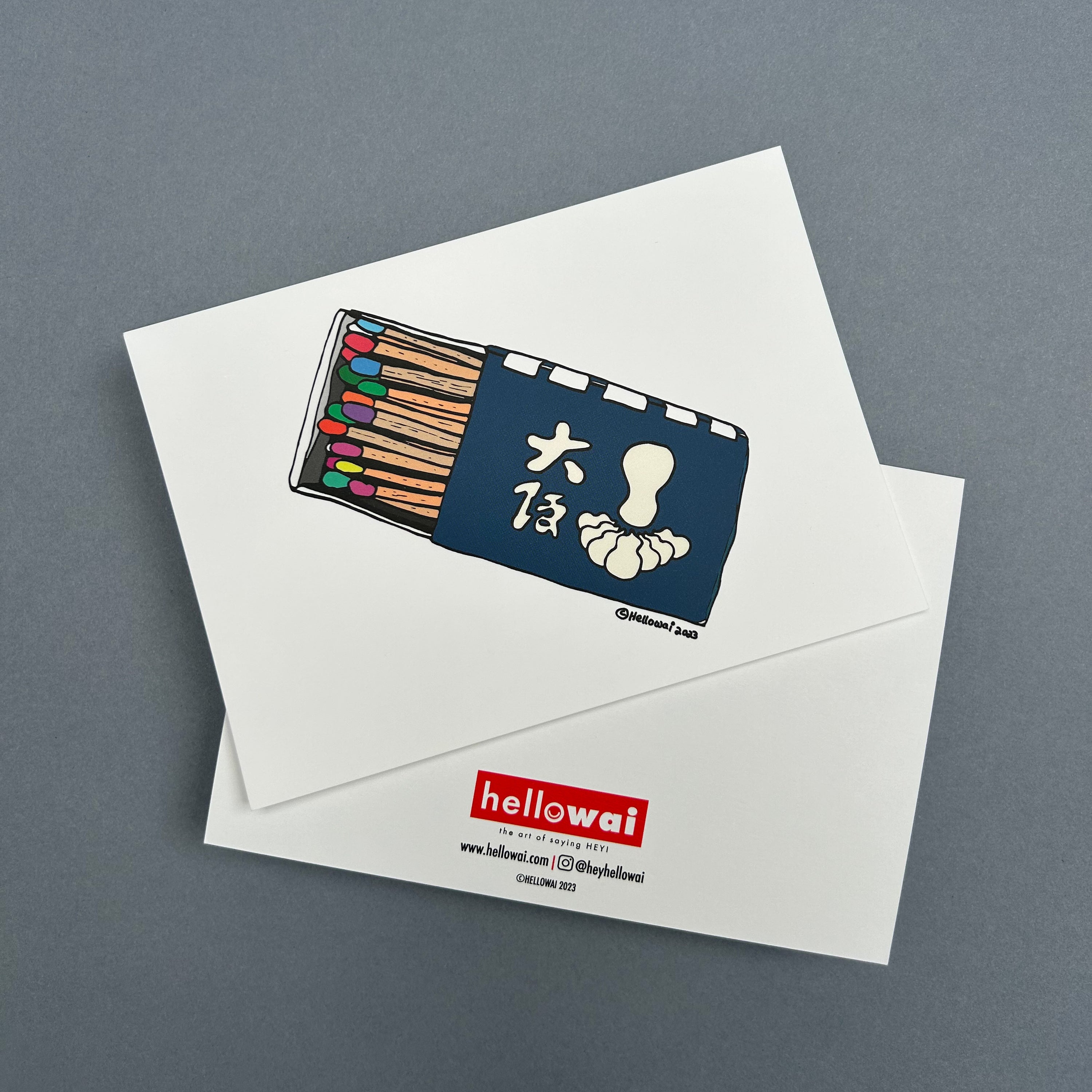 Front and back view of an A6 Hello Wai flat notecard. Front has colour illustration of a half opened restaurant matchbox containing matchsticks with different coloured heads. Back has the Hello Wai logo.
