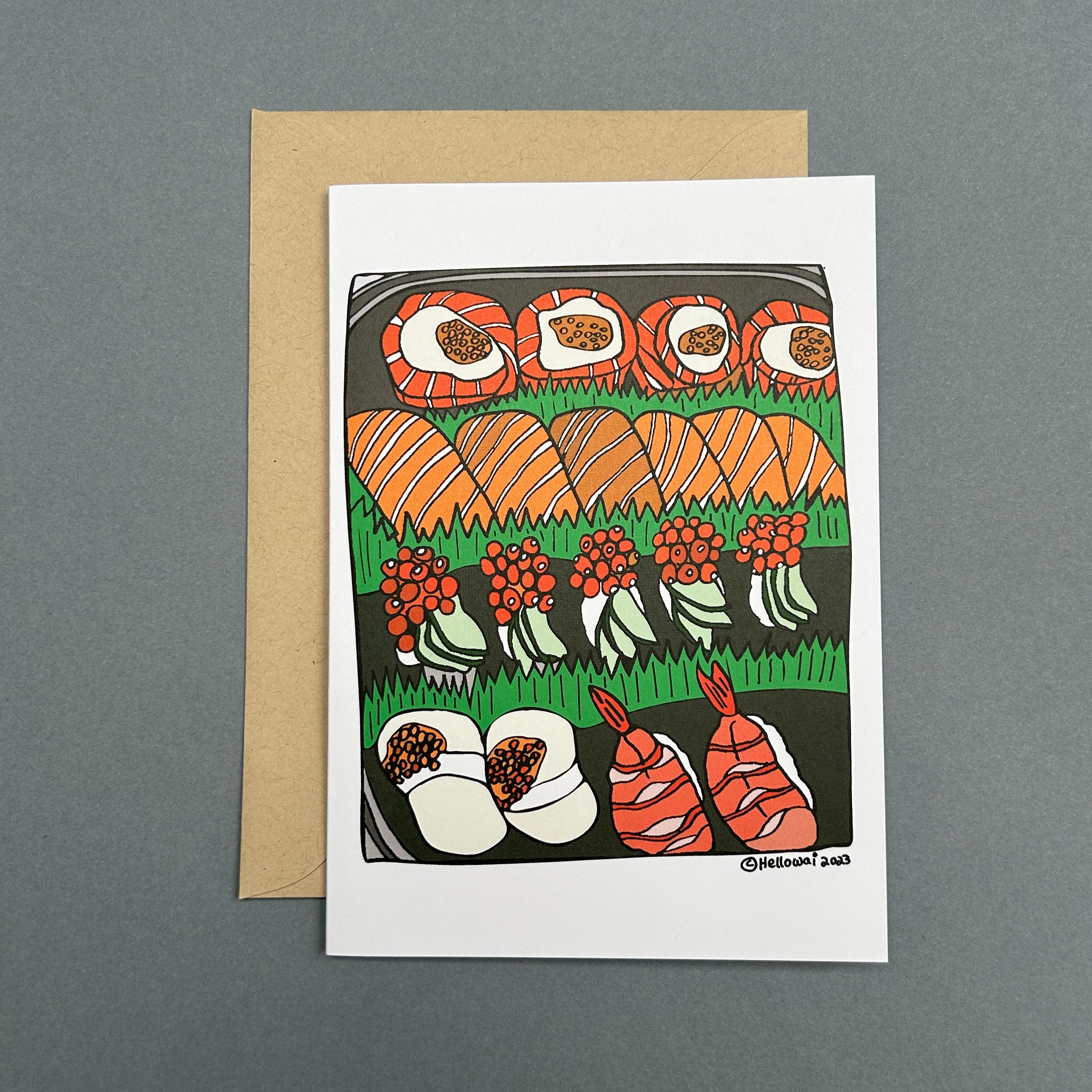 An A6 Hello Wai folded greeting card with a colour illustration of a sushi platter with five different types of sushi rolls, printed on white card. The card is placed on top of a brown envelope.
