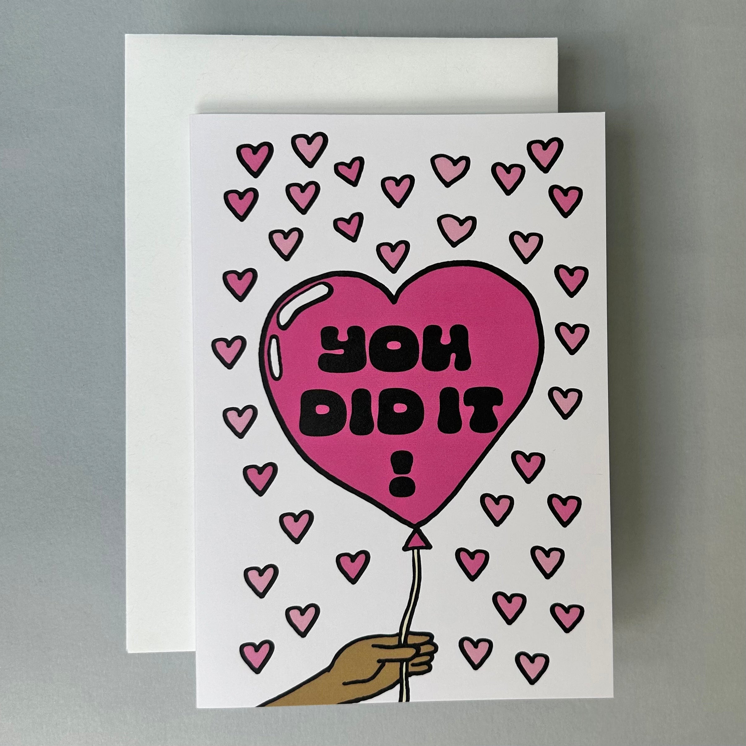 Greeting card with a pink balloon shaped like a heart with 'YOU DID IT!' text, surrounded by small hearts, on a gray background.