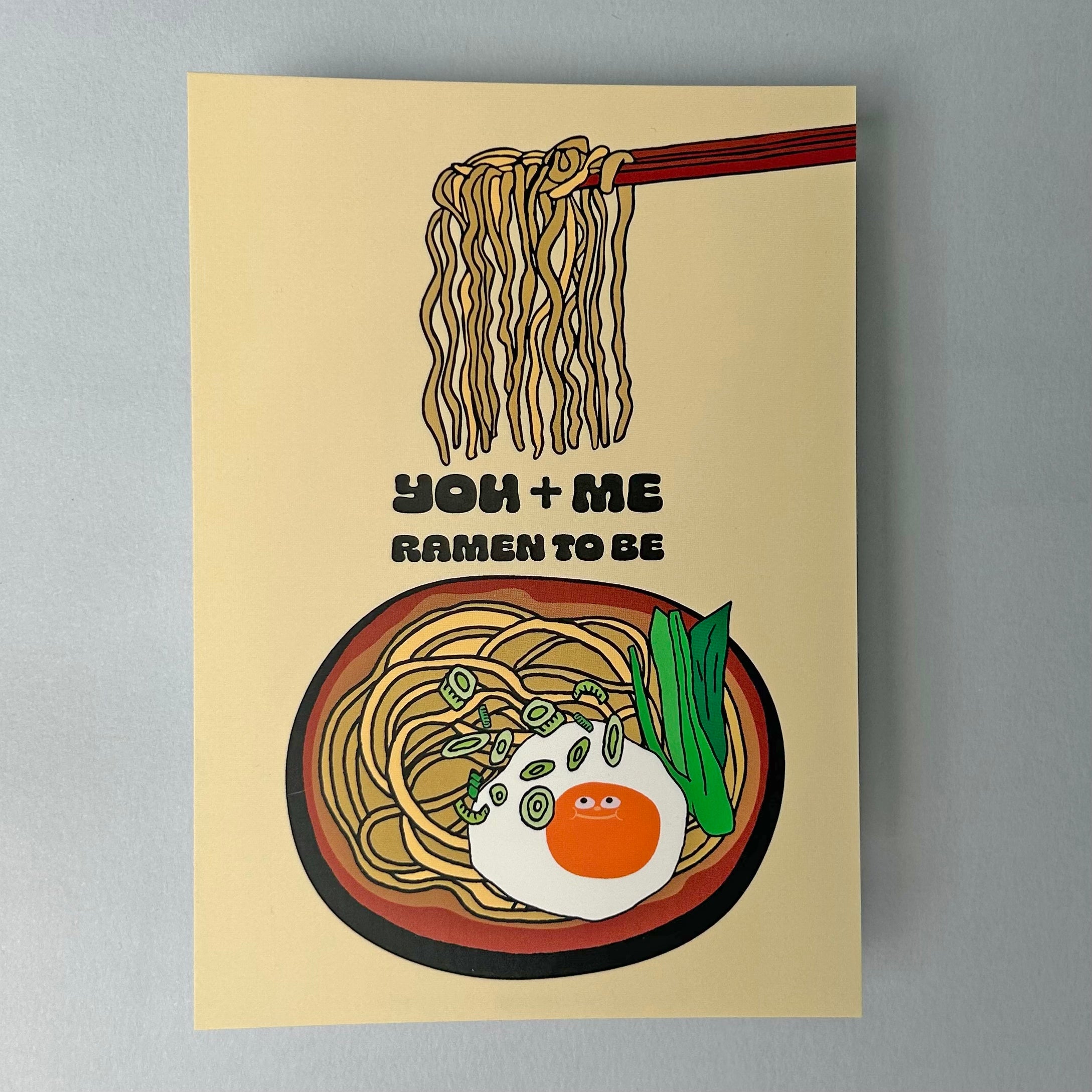 A notecard with an illustration of a ramen noodle bowl with the text 'YOU + ME RAMEN TO BE' 