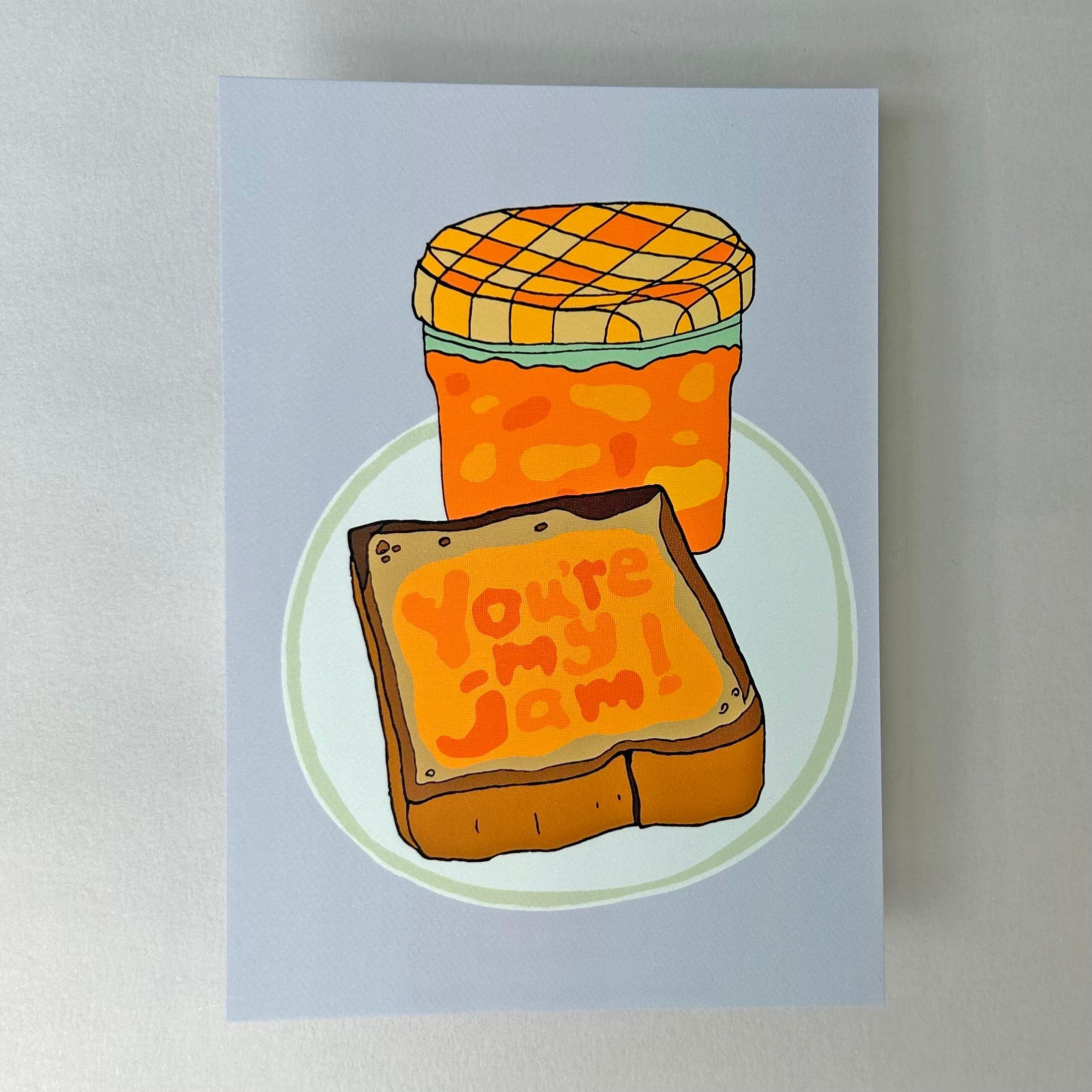 A notecard with a illustration of a jar of jam and a piece of bread with the words 'You're My Jam' written on it against a light blue background. 